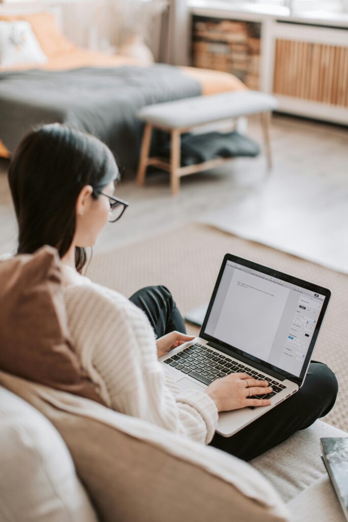 From above back view of unrecognizable female in casual wear typing on keyboard of laptop while working at home remotely